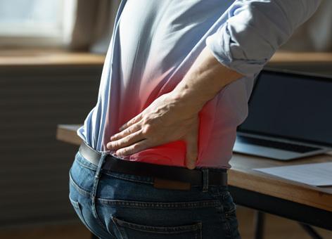 Close up rear view stressed young man touching lower back feeling discomfort, suffering from sudden pain due to sedentary lifestyle or long computer overwork in incorrect posture at home office.